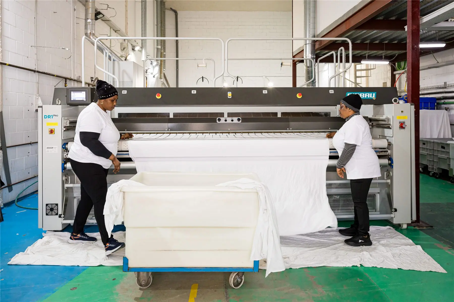 Worker loading white linen into a trolley next to the ironer