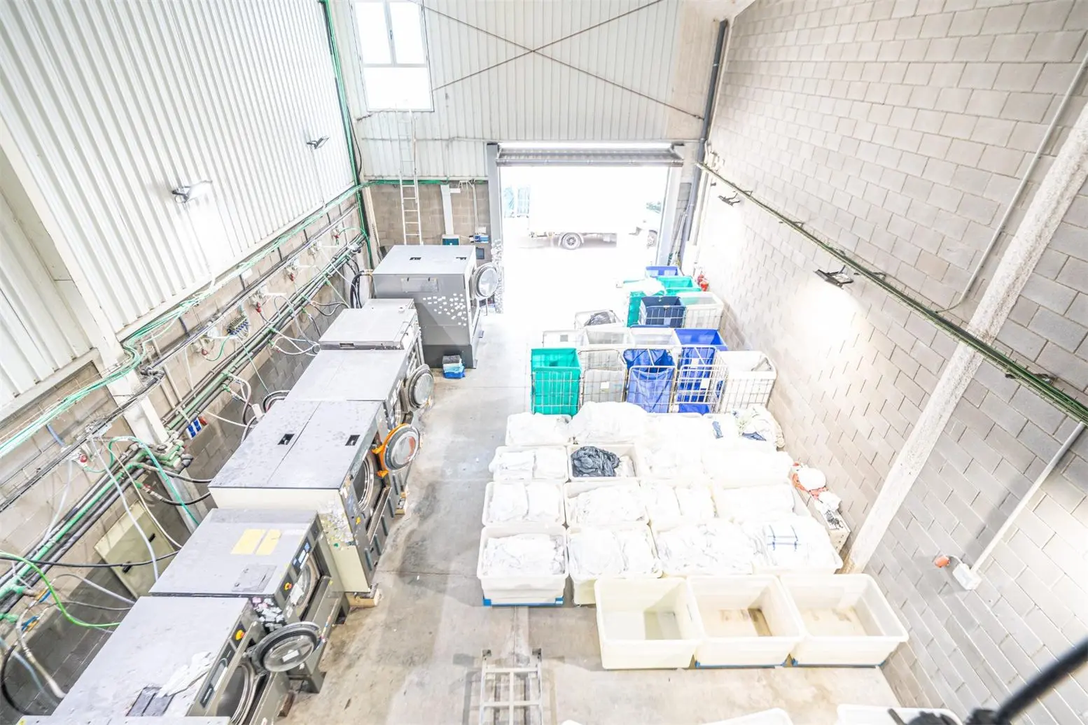 The plant seen from above: industrial washing machines on one side and boxes of linen in the middle